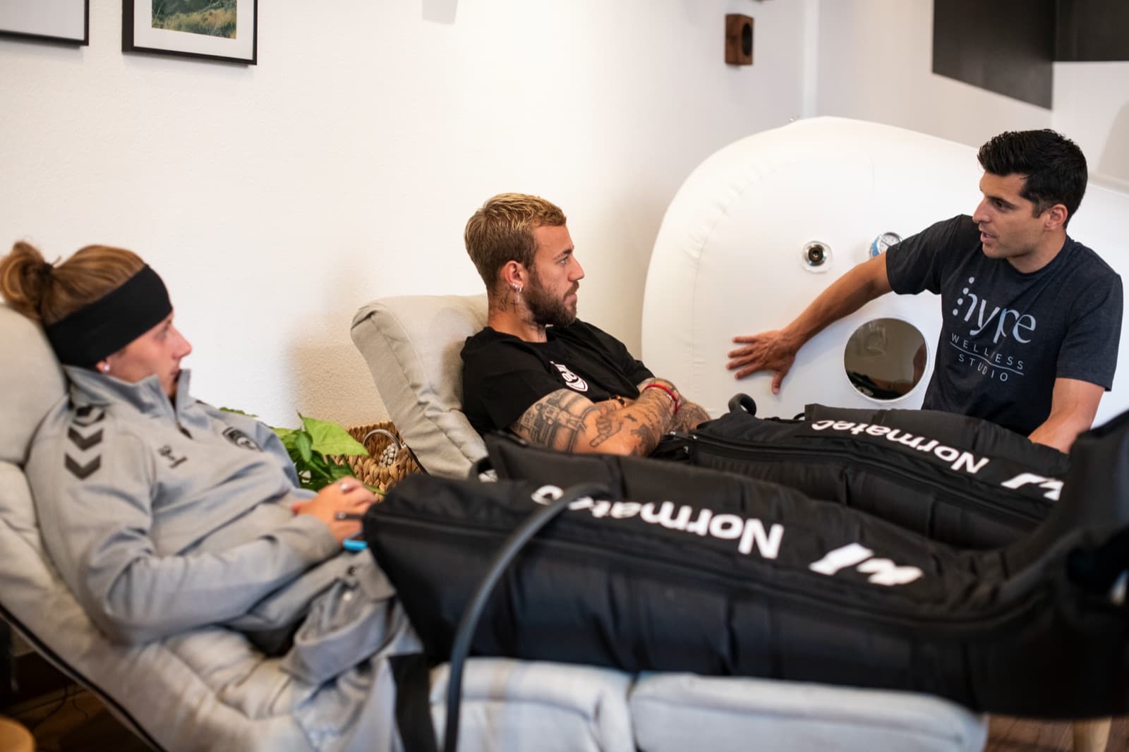 A staff member consulting with members relaxing in recovery chairs with compression boots